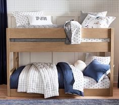 two bunk beds with blue and white bedding in a small room next to a window