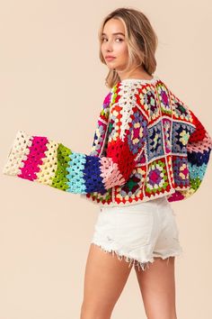 a woman in white shorts and a colorful crochet sweater is posing for the camera