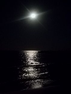 the moon is shining over the ocean at night