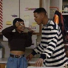 two people standing in a kitchen, one is brushing the other's teeth