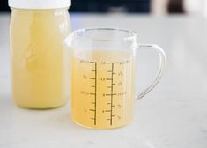 a measuring cup with liquid in it next to a glass jar filled with liquid on a counter