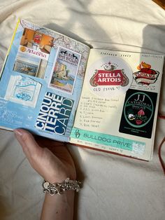 a person is holding an open book in their hand on a bed with white sheets