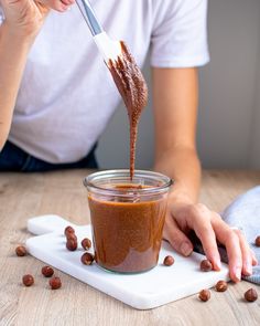 a woman is pouring chocolate into a jar with nuts on the table next to her