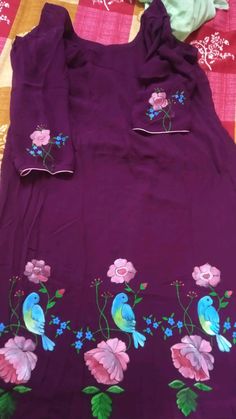 a purple dress with blue birds and pink flowers on the bottom is laying on a bed