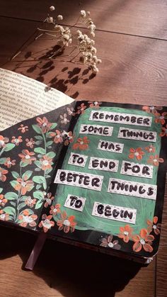 an open book sitting on top of a wooden table next to a plant and flowers