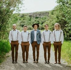 a group of men standing next to each other in front of trees and dirt road