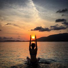 a person sitting in the water with their hands up at sunset or sunrise, while the sun is setting