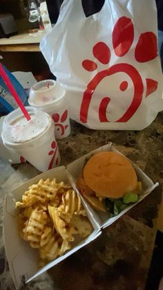 a hamburger and french fries are sitting on a table next to a bag of sodas