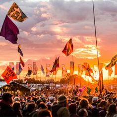 a crowd of people standing around flags flying in the air at an outdoor music festival