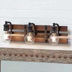 three light fixtures mounted on a wooden frame with metal fittings and glass globe bulbs