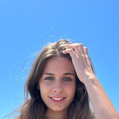 a woman with long hair is smiling and holding her hand up to her head while standing in front of the blue sky