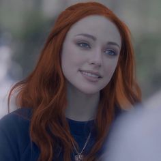 a close up of a person with red hair and blue eyes wearing a black shirt