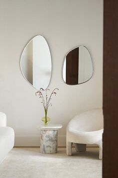 two round mirrors on the wall above a table with a vase and flower in it