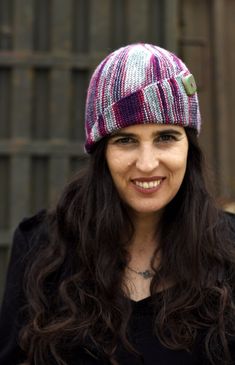 a woman with long hair wearing a knitted hat and smiling at the camera while standing in front of a fence