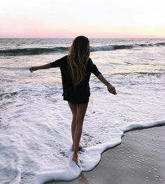 a woman walking on the beach at sunset