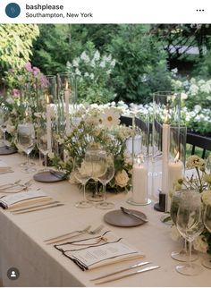 the table is set with wine glasses, silverware and flowers in glass vases