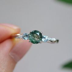 a person holding an engagement ring with a green and blue stone on it's side