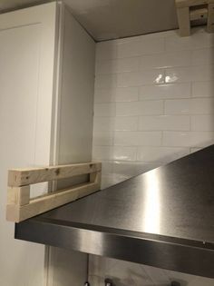 a metal counter top in a kitchen with white tiles on the wall and cupboards behind it