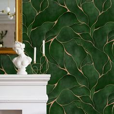 a white fireplace with a green wallpaper behind it and a gold framed mirror on the mantle