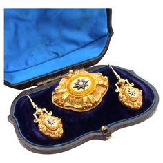 A Victorian suite of jewellery, comprising a brooch and a pair of earrings, each set with a seed pearl, with enamel detailing, in 18 karat yellow gold, with 9 karat yellow gold fittings (brooch pin and ear hooks). This striking antique jewellery suite is truly beautiful to behold, made even more special by the fact that each piece has survived, and is still presented in its original purple velvet and blue satin lined fitted case. The brooch is set to the centre with a shimmering seed pearl. The pearl is set to the centre of an 8-pointed star, which is surrounded by a border of cobalt blue enamel. The star sits at the centre of an oval shaped panel, which is surrounded by borders of twisted rope. The lozenge shaped brooch is adorned with beading and glorious twisted rope wirework, creating Glass Locket, Gold Pin, Enamel Brooch, Purple Velvet, Seed Pearl, Blue Satin, Pearl Size, Pure Gold, Antique Jewellery