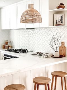 three stools sit at the counter in this kitchen with white cabinets and tile backsplash