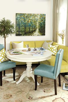 a white table topped with blue chairs next to a yellow couch and painting on the wall