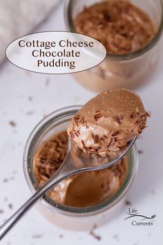 two jars filled with chocolate pudding on top of a white table next to a spoon