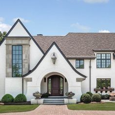 a large white house with black trim and windows on the front door is surrounded by greenery