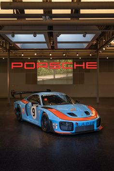 a blue and orange race car parked in front of a sign that reads porsche he