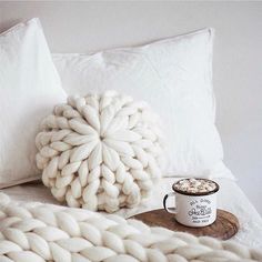 a cup of coffee sitting on top of a bed next to a blanket and pillow