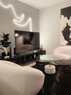 a living room with two white chairs and a black table in front of a tv