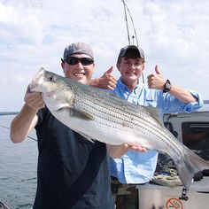 two men on a boat with a large fish in their hands and one man giving the thumbs up