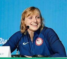 a woman sitting at a table with a microphone in front of her and a blue wall behind her