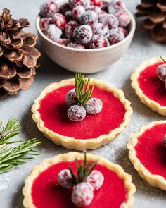 small tarts with berries and pine cones on top, surrounded by pine cones in the background