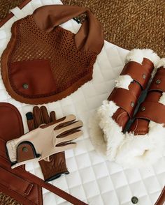 a pair of brown gloves sitting on top of a white blanket next to a purse