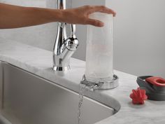 a person's hand is pouring water from a faucet into a sink