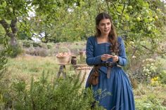 a woman in blue dress standing under an apple tree