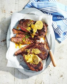 two steaks on a plate with yellow sauce and mustard next to a blue towel