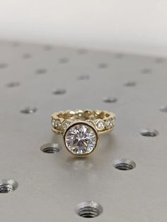 a gold ring with two diamonds on the side and one diamond in the middle, sitting on top of a metal surface