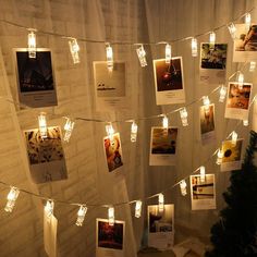 some lights are hanging on a wall with pictures attached to the string and tags strung from them