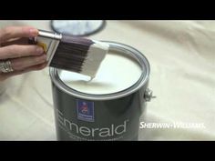 a person holding a paint brush over a can of white paint