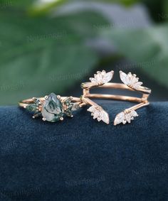 two gold rings with green and white stones sitting on top of a blue velvet surface