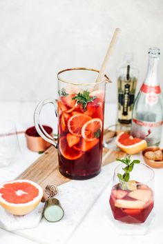 a pitcher filled with liquid sitting on top of a cutting board next to sliced fruit