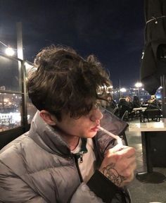 a man sitting at a table eating food and drinking from a cup with a straw in his mouth