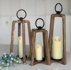 three wooden lanterns with lit candles in them sitting on a table next to eucalyptus branches