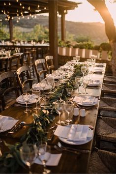 a long wooden table with place settings and plates on it in front of an outdoor dining area