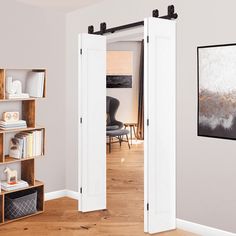 an open door leading to a living room with white walls and wooden floors, in front of a painting on the wall