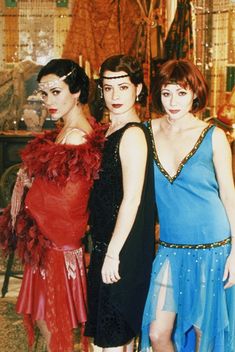 three women standing next to each other wearing dresses with feathers on the bouds