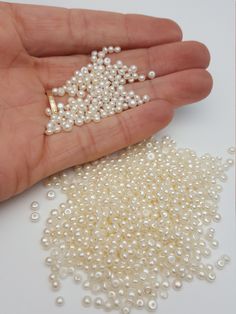 a hand holding some pearls in it's palm next to another white bead