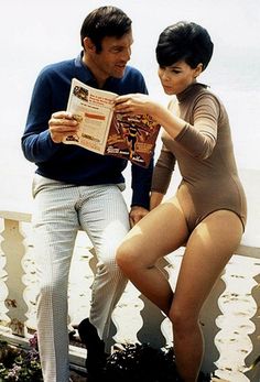 a man and woman sitting next to each other on a balcony reading a magazine together